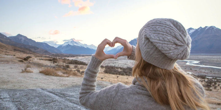 Lady holding up her hands to make a heart with mountains in the background