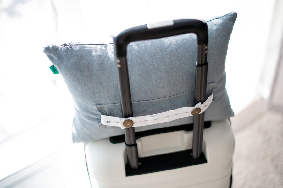 A Kind Face Cloud Wool Travel Pillow Hooked by Its Handy Strap Onto a Travel Suitcase's Arm Extension that's used for Wheeling the Suitcase